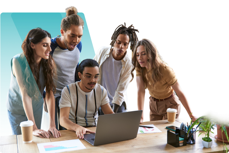 A diverse group of young professionals gathered around a laptop at a wooden desk, engaged in discussion and teamwork in a modern office setting. Documents with bar charts and takeaway coffee cups are visible on the table.